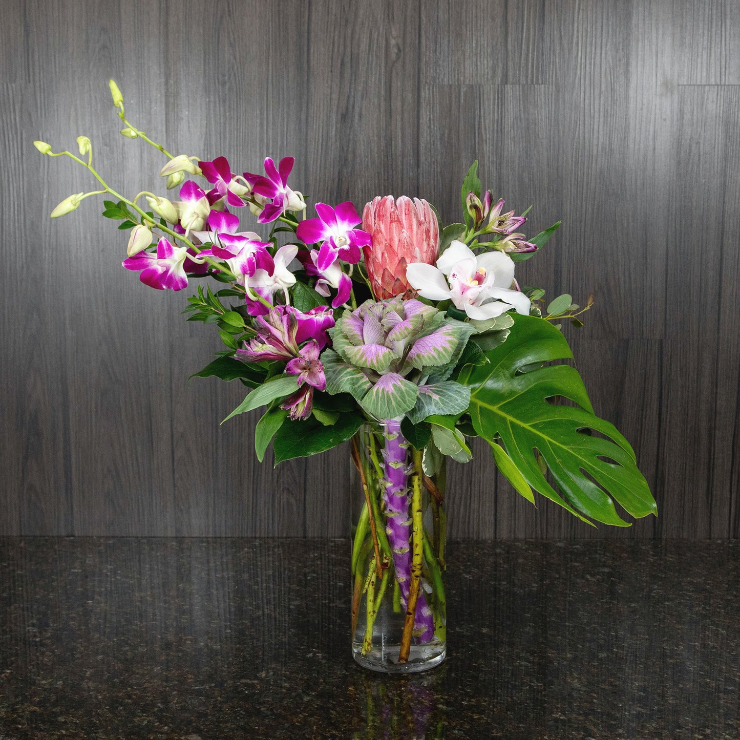 a tropical flower arrangement in a tally glass cylinder