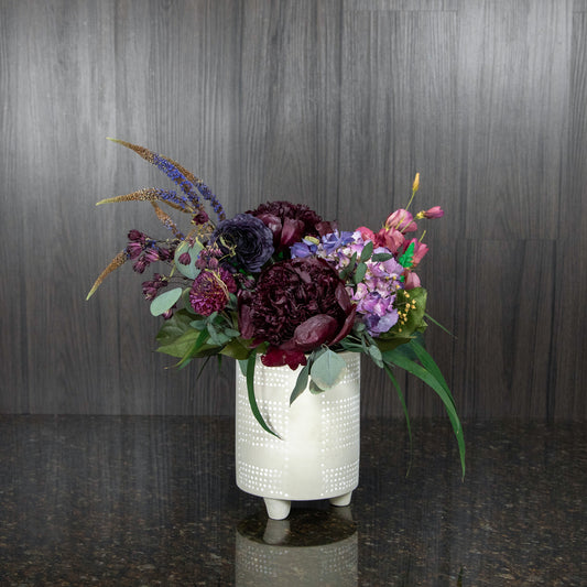 a floral arrangement made out of dried flowers in dark shades of purple, burgundy, and pink