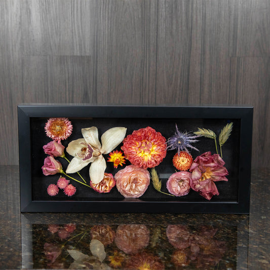 a black shadow box filled with a variety of colorful dried flower blooms