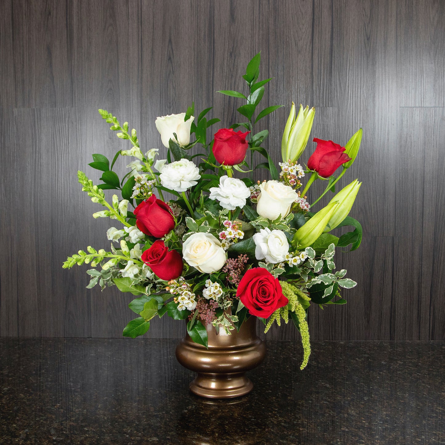 a tabletop funeral spray with red and white flowers in a copper plastic urn container