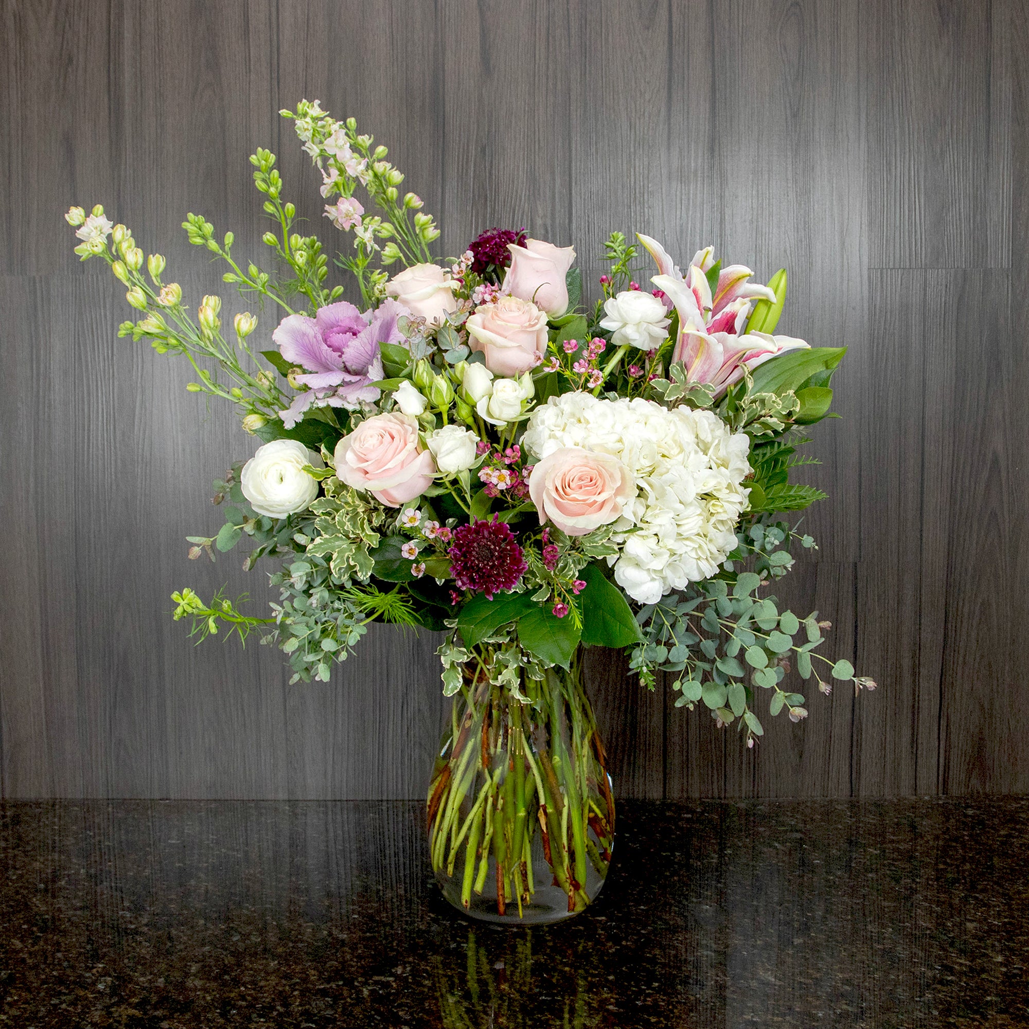 a large flower arrangement with a mix of pastel and spring flowers in a glass vase