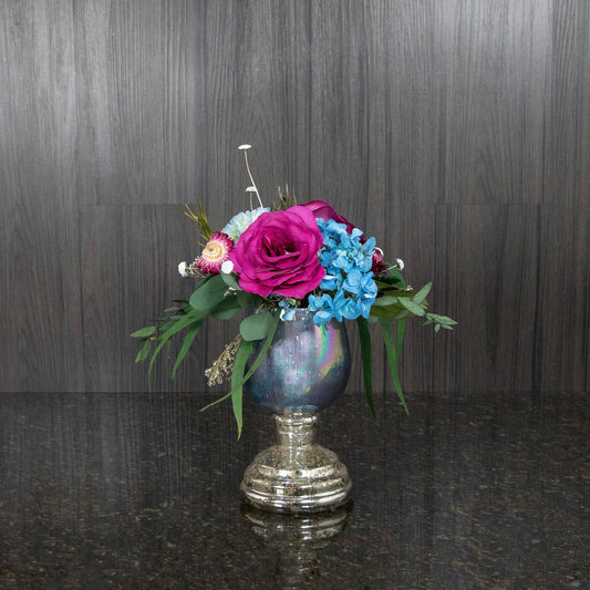 a dried floral arrangement featuring dried pink and blue flowers with dried greenery