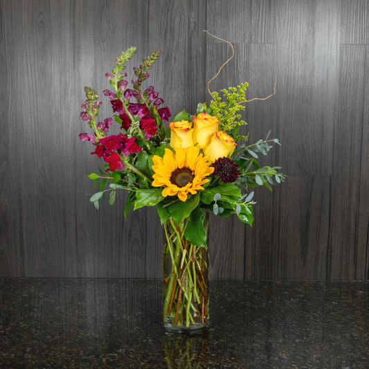 a contemporary flower arrangement of reds and yellow in a glass cylinder vase