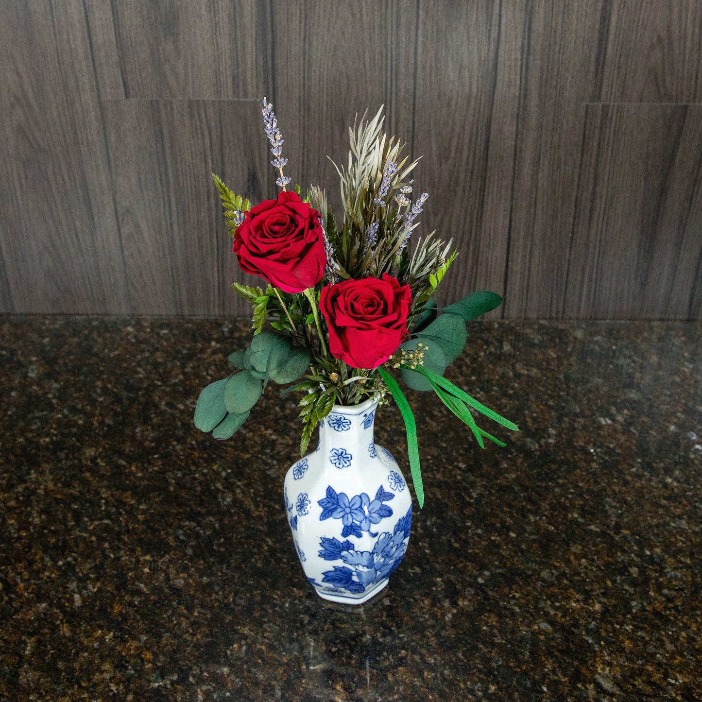 top down view of two red preserved roses with dried greenery in a white and blue ceramic vase