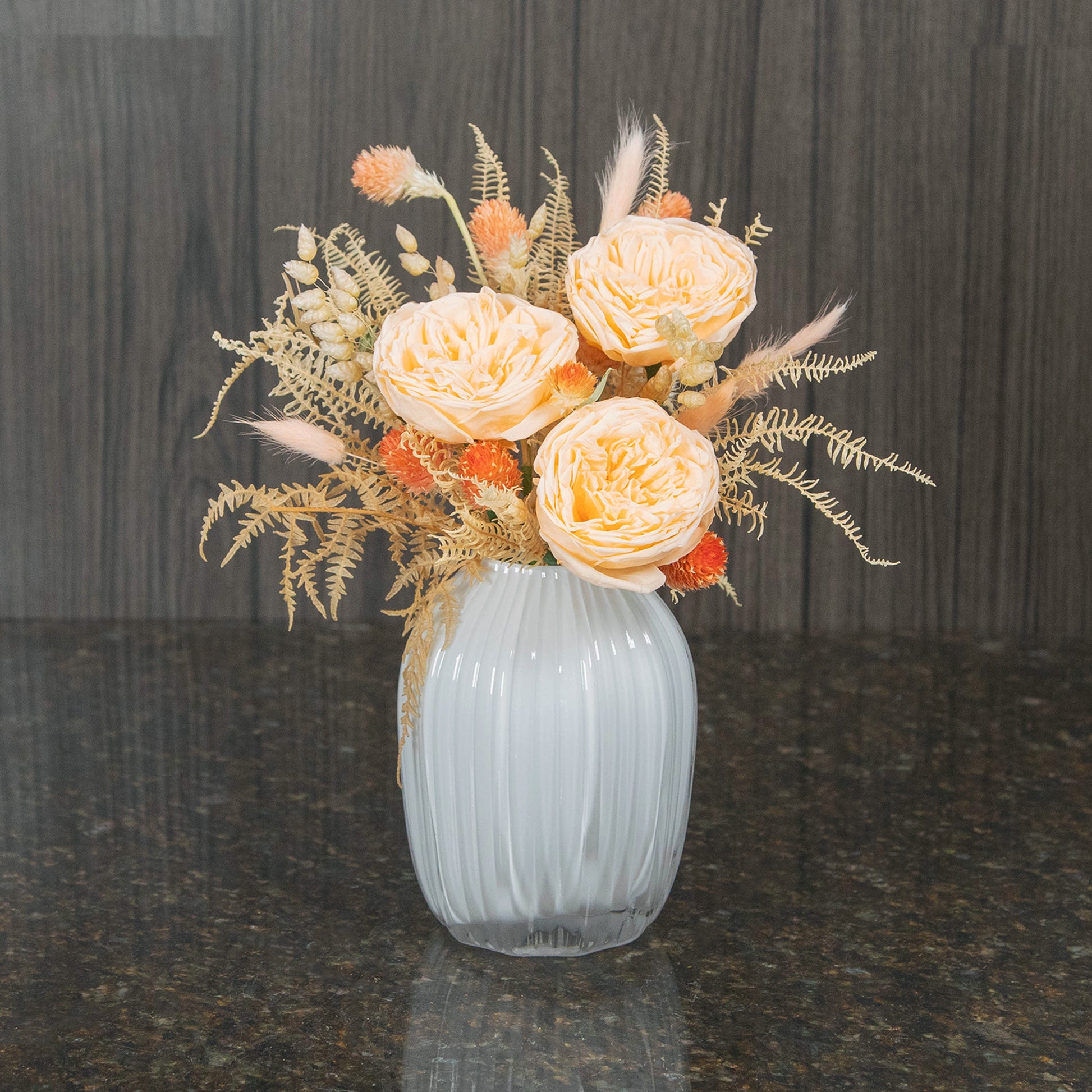 three peach preserved garden roses with bleached greenery in a white glass vase