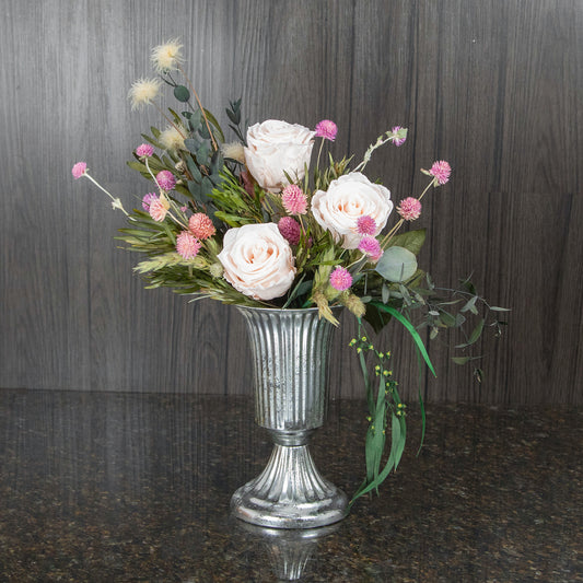 three blush preserved roses and dried greenery and filler in a silver footed metal vase