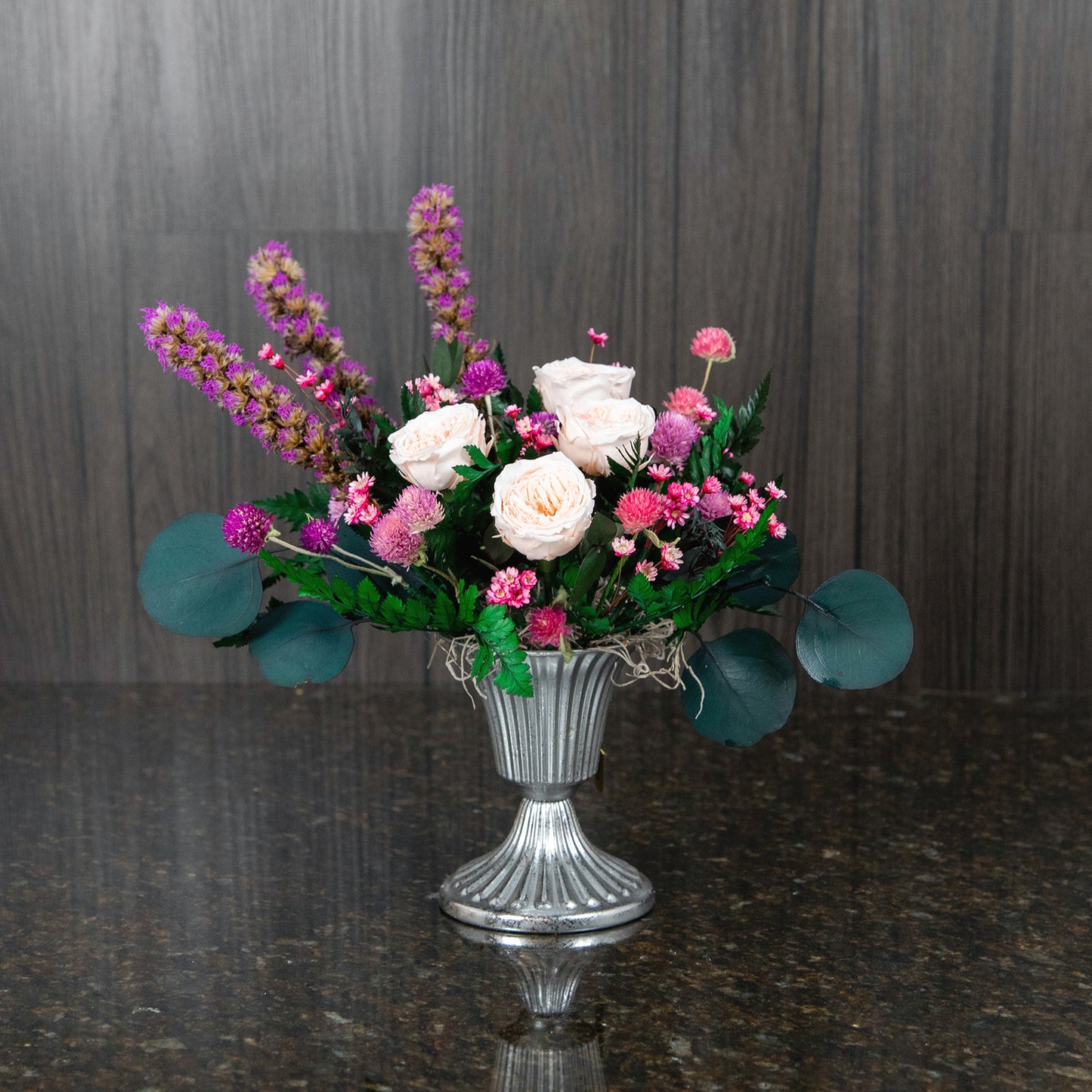 peach preserved garden roses and other dried flowers and greenery in a silver footed metal vase