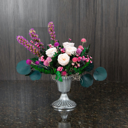 peach preserved garden roses and other dried flowers and greenery in a silver footed metal vase