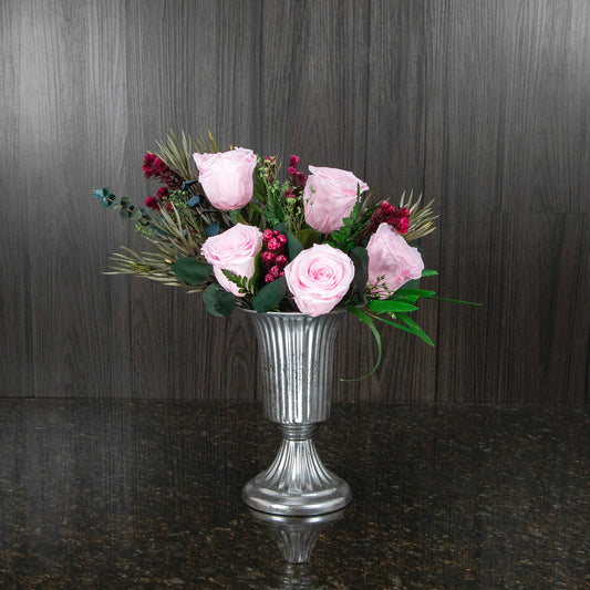 five pink preserved roses and dried greenery in a footed silver metal vase