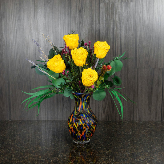 five yellow preserved roses and dried greenery in a colorful glass vase