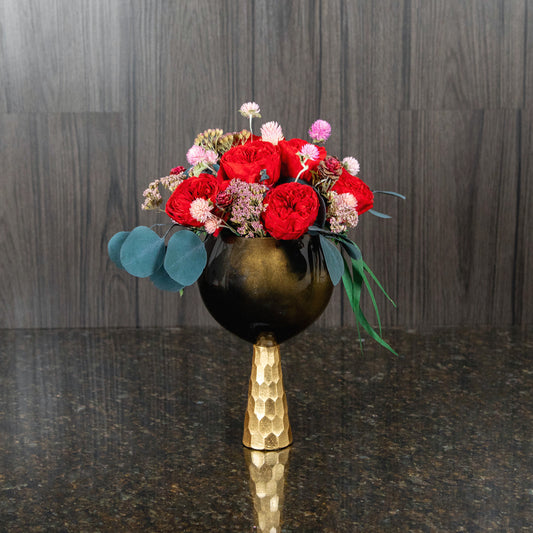 preserved red garden roses and other dried flowers and greenery in a black and gold glass vase
