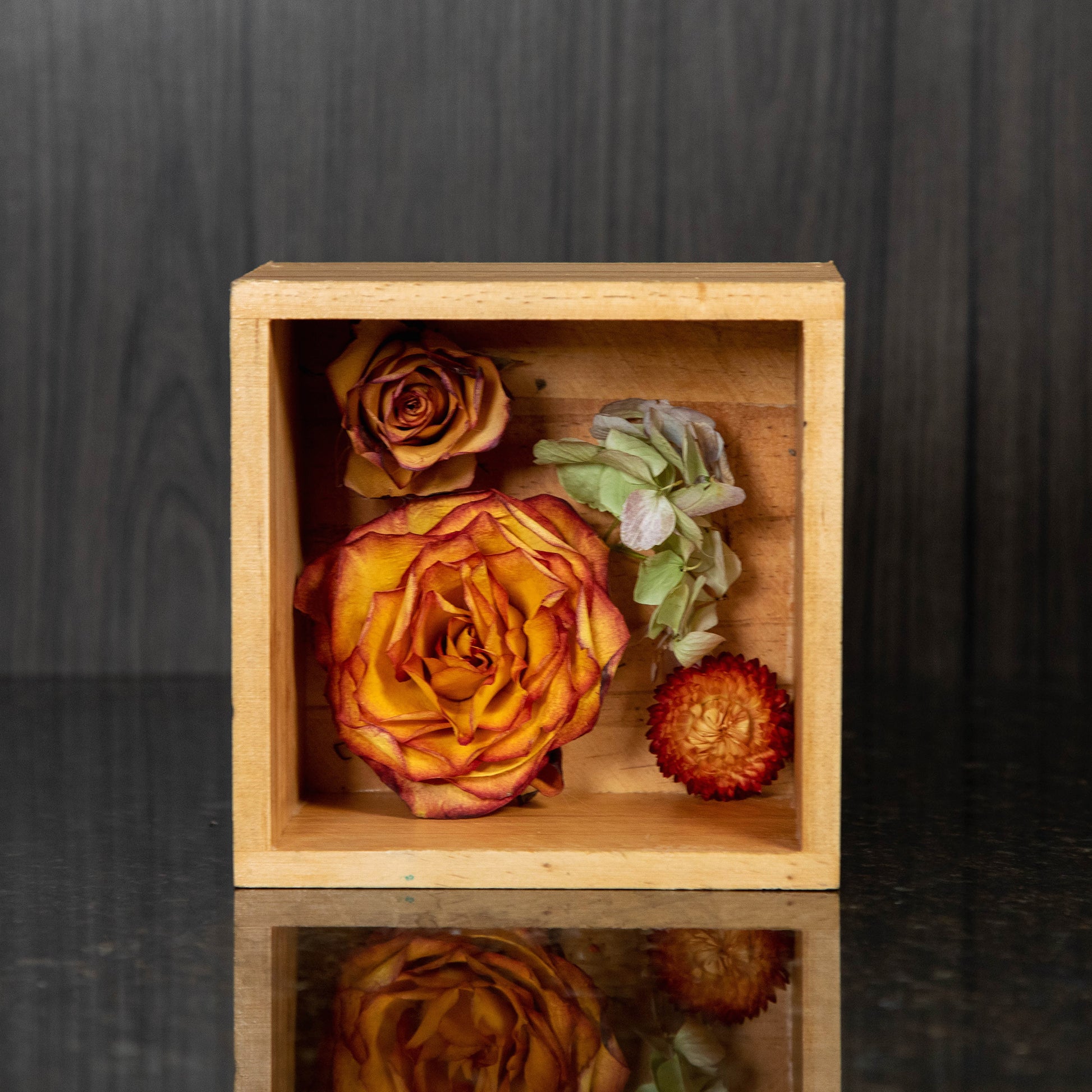 a wooden shadow box with a few dried flowers inside of it