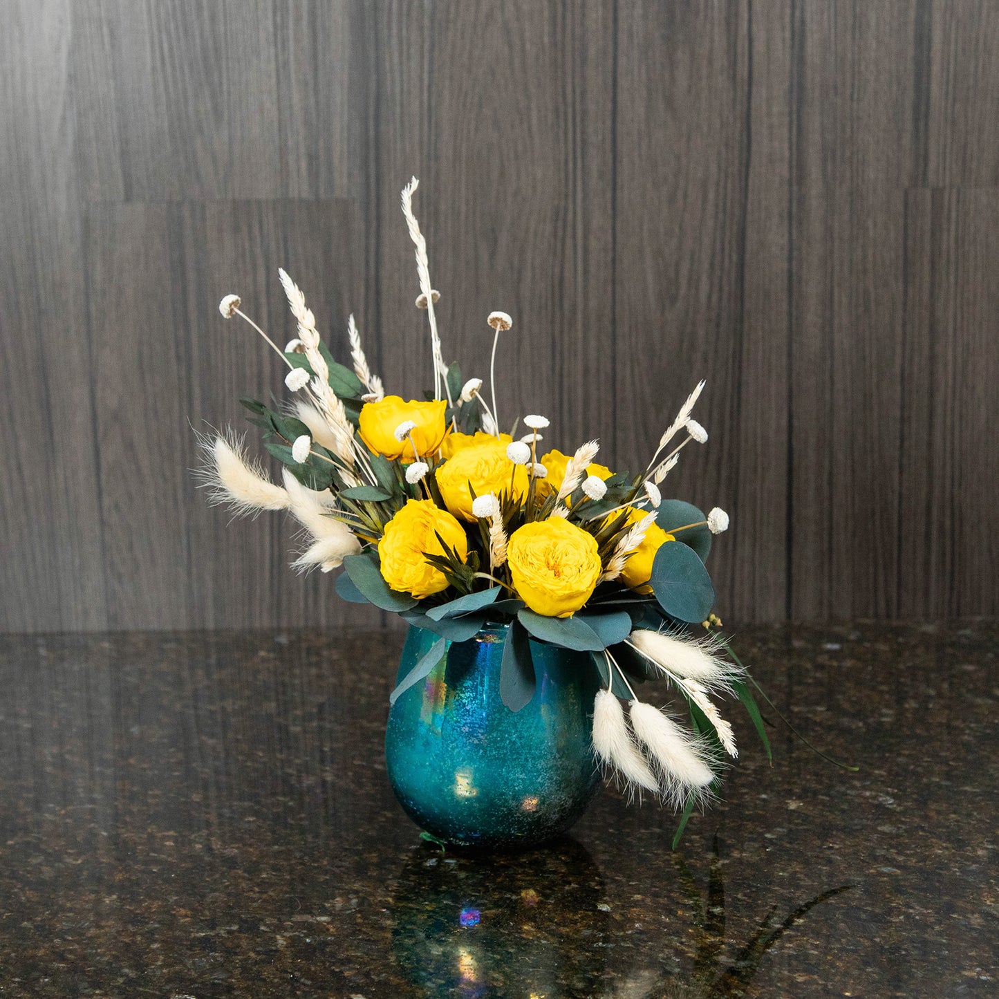 petite yellow preserved garden roses in a round blue vase with dried greenery and filler