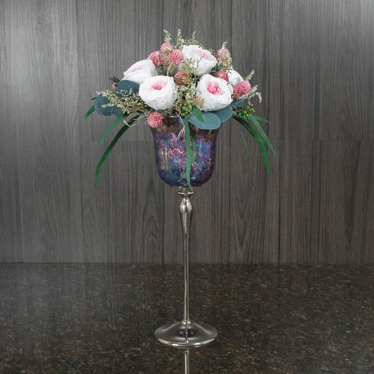 pink preserved garden roses, dried greenery, and filler in a tall stemmed glass vase