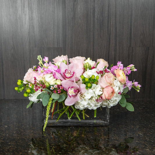 a compact flower arrangement with white, pink and green flowers in a glass rectangular vase