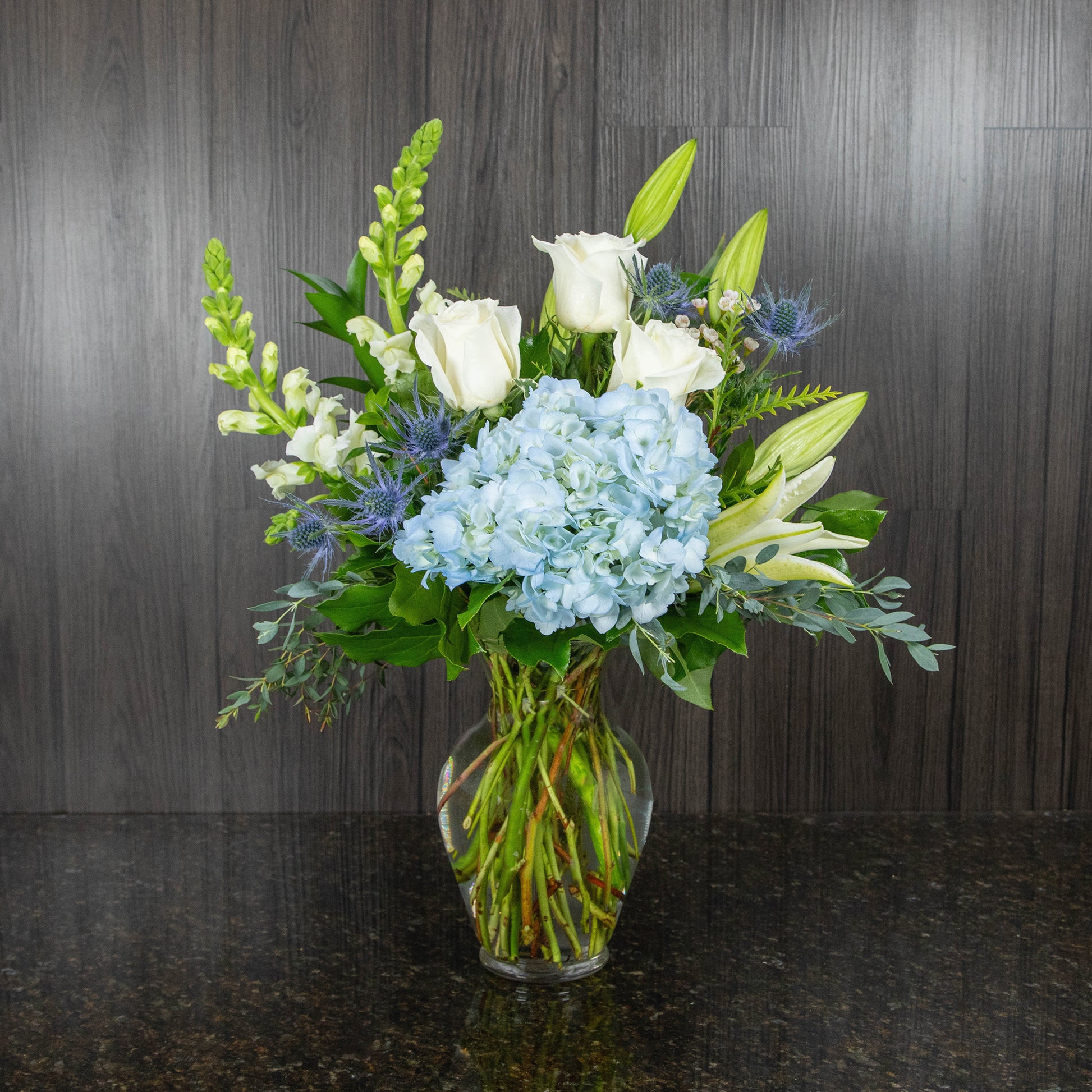 a flower arrangement of white and blue flowers in a glass vase