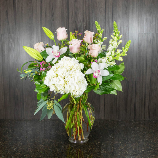 a flower arrangement with white and pink flowers in a tall urn shaped glass vase