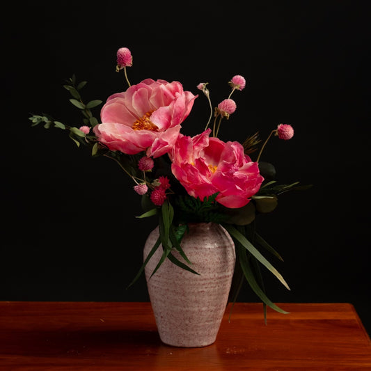 Two dried peonies, gomphrena, and greenery in a pink ceramic vase