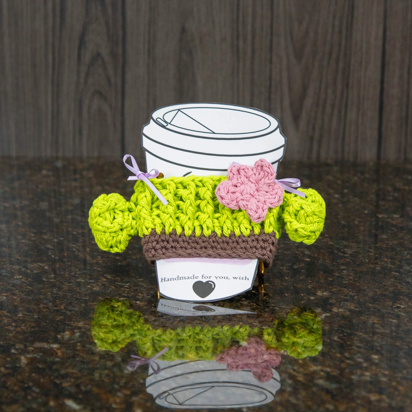 a crochet cup cozy that looks like a cactus - bright green with a light pink flower
