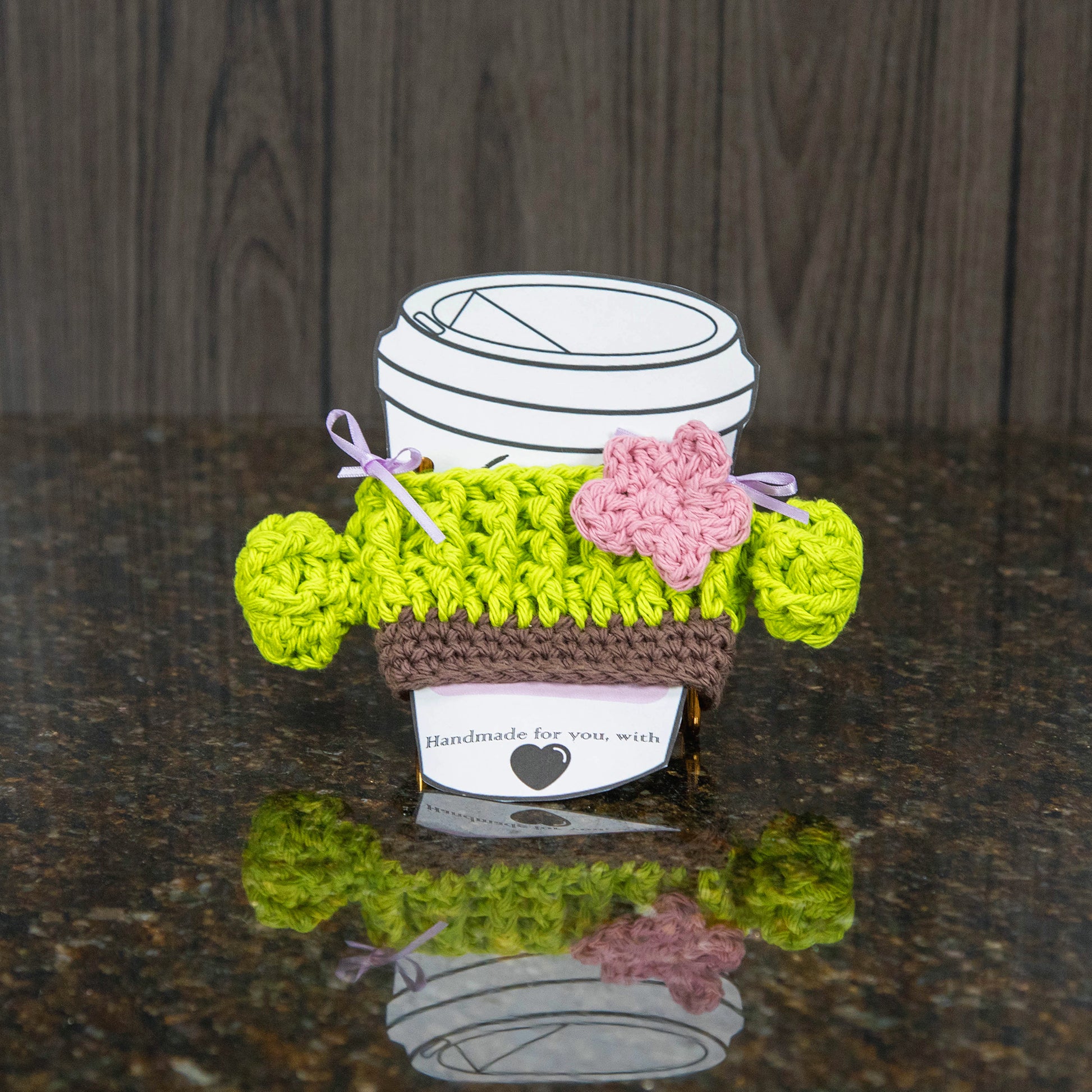 a crochet cup cozy that looks like a cactus - bright green with a light pink flower