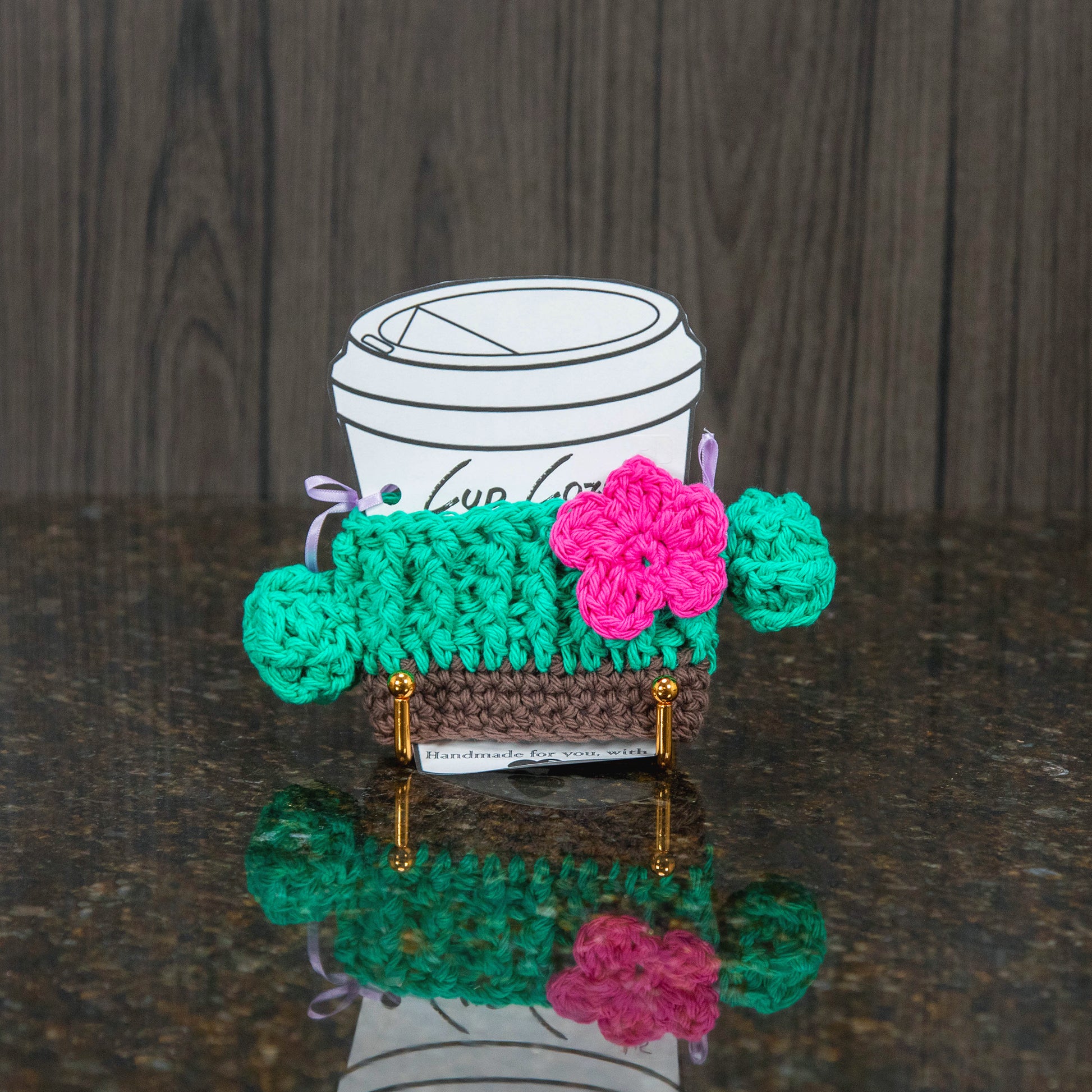 a crochet cup cozy that looks like a cactus - green with a magenta flower