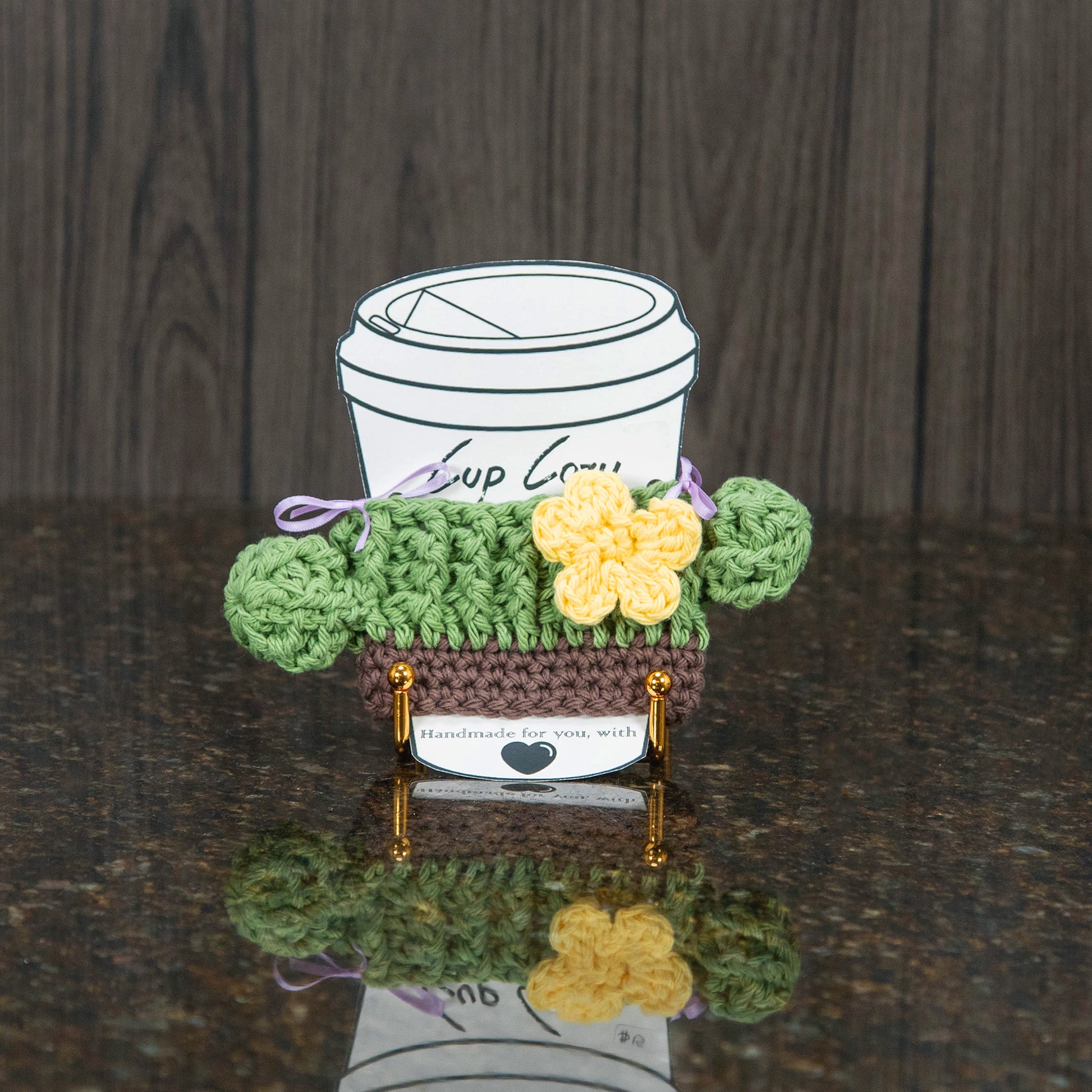 a crochet cup cozy that looks like a cactus - sage green with a yellow flower