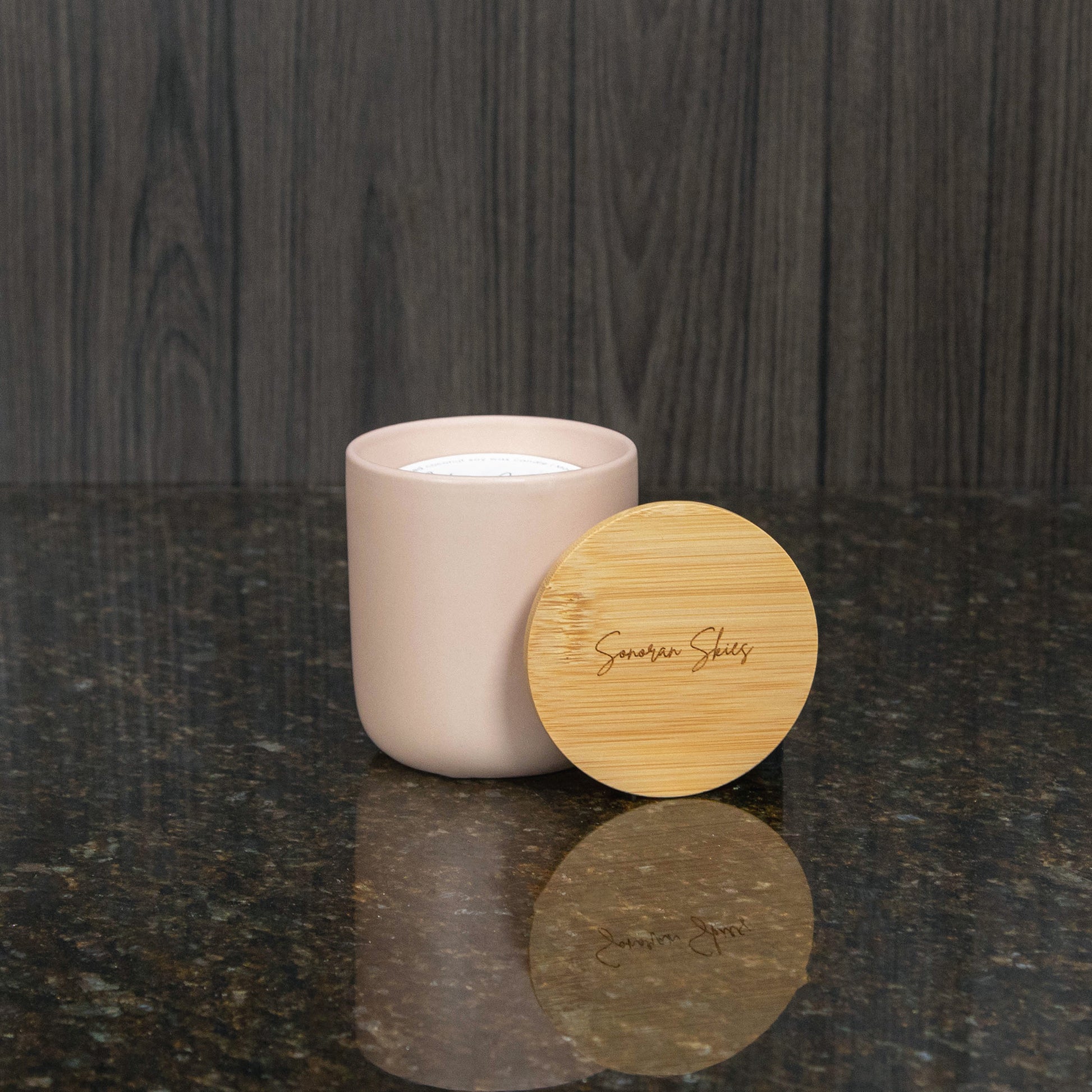 a candle in a blush container with a lid that reads Sonoran Skies