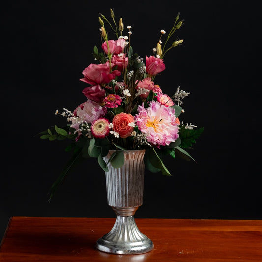 a mix of dried flowers and greenery in a silver footed metal vase