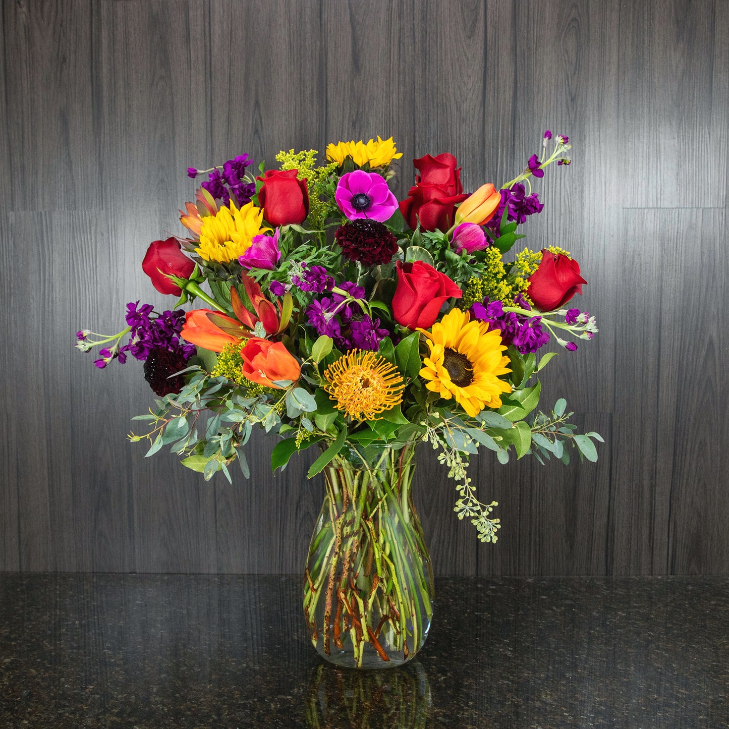 a mix of bright, deep jewel tone flowers in a glass vase