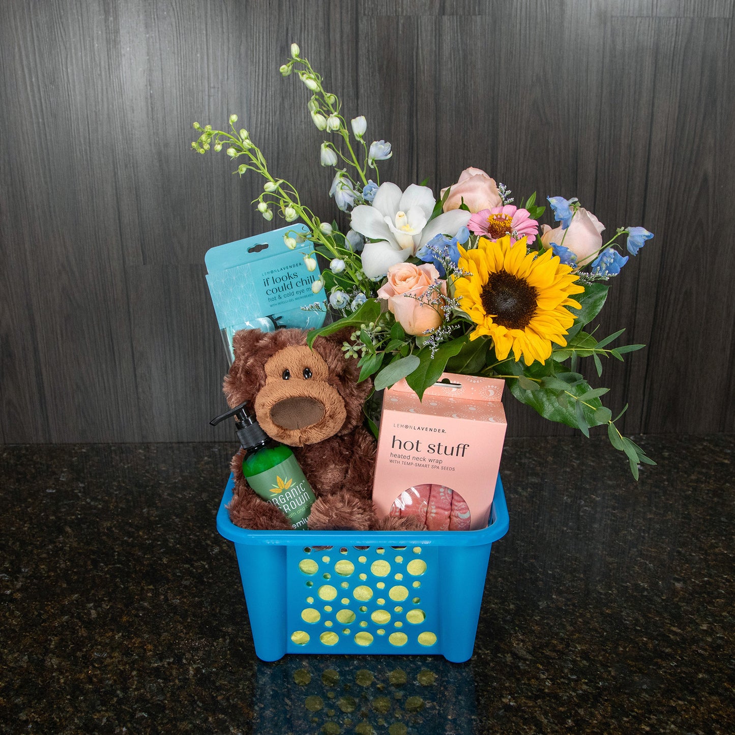 a gift basket containing a flower arrangement, a teddy bear, and other gifts