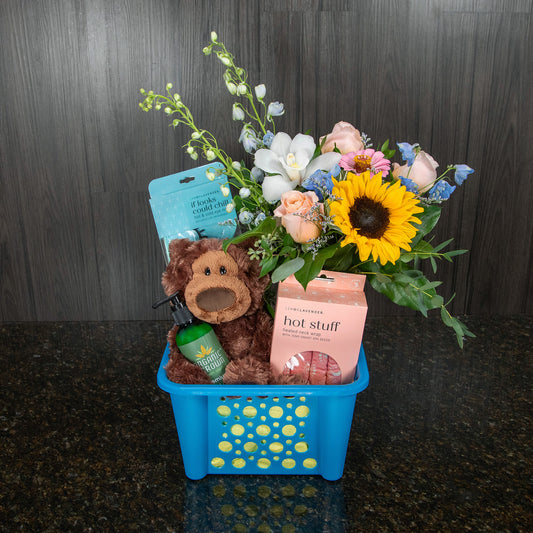 a gift basket containing a flower arrangement, a teddy bear, and other gifts