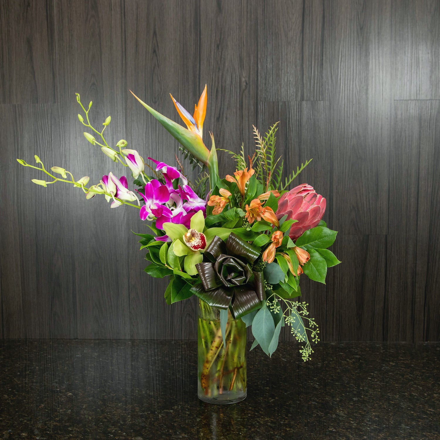 a contemporary flower arrangement with a mix of tropical flowers in a glass cylinder vase