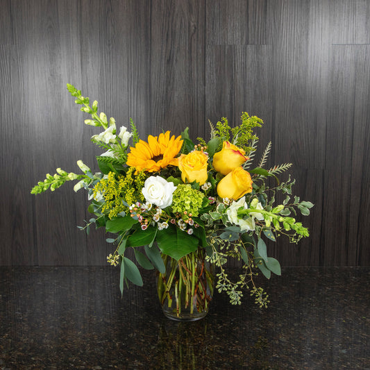 a flower arrangement with white, yellow, and green flowers in a potbelly glass vase