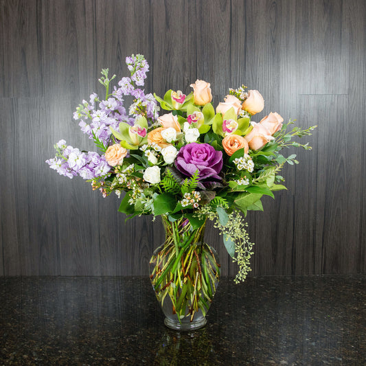 a large flower arrangement with a mix of pastel flowers in a glass vase