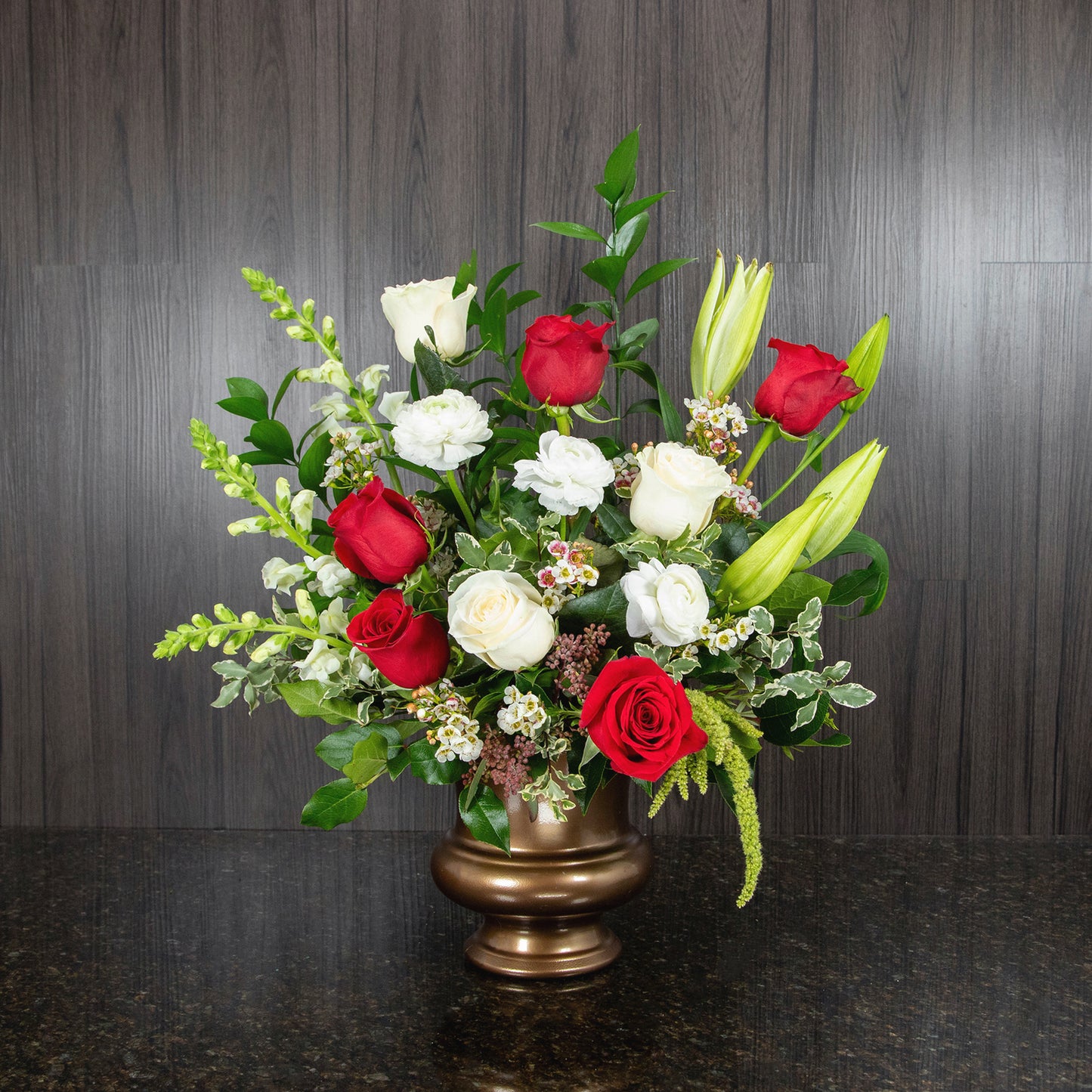 a tabletop funeral spray with red and white flowers in a copper plastic urn container