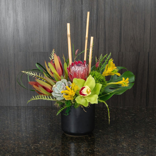 a colorful tropical flower arrangement in a black ceramic pot
