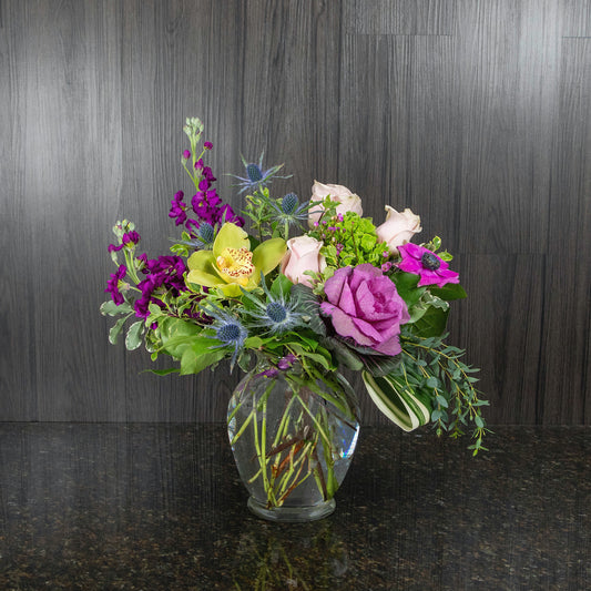 a mix of different types of flowers in an urn shaped glass vase