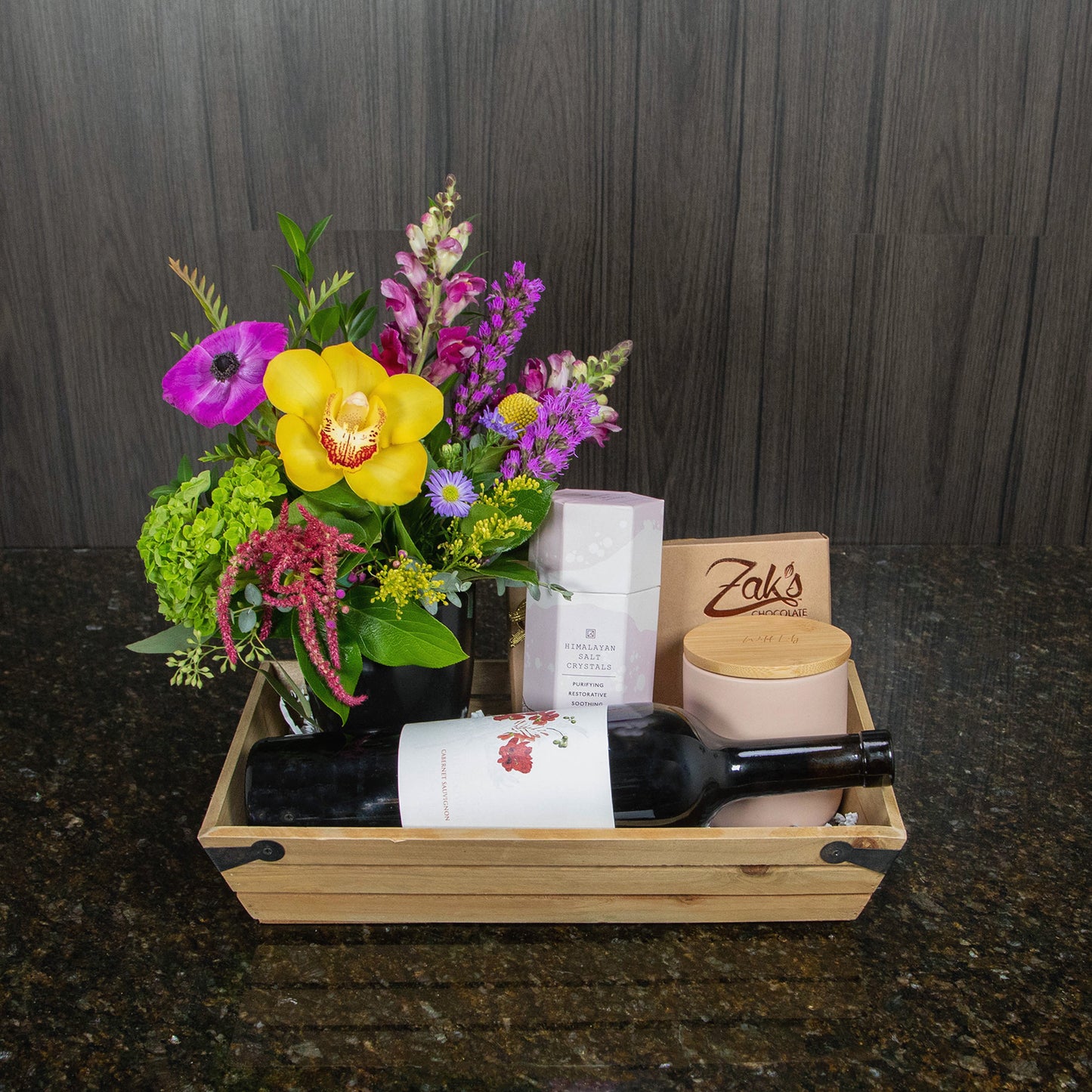 a gift basket with flowers, wine, a candle, chocolates, and salt crystals