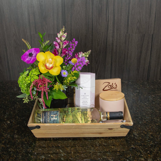 a gift basket with flowers, wine, a candle, chocolates, and salt crystals