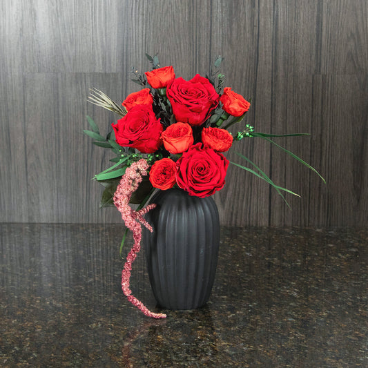red preserved roses and garden roses with dried greenery and filler in a black vase