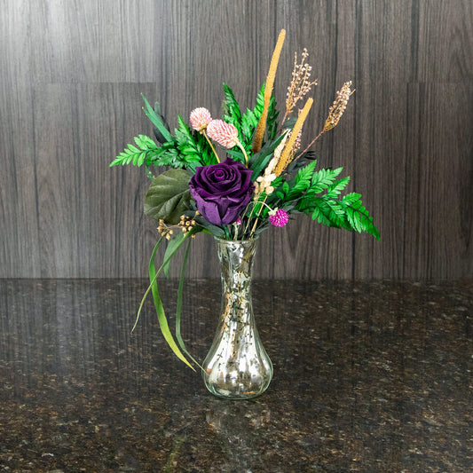 a single dark purple preserved rose and dried greenery in a silver mercury glass bud vase