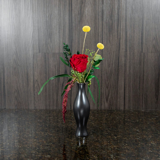 a single burgundy preserved roses and dried greenery in a black bud vase