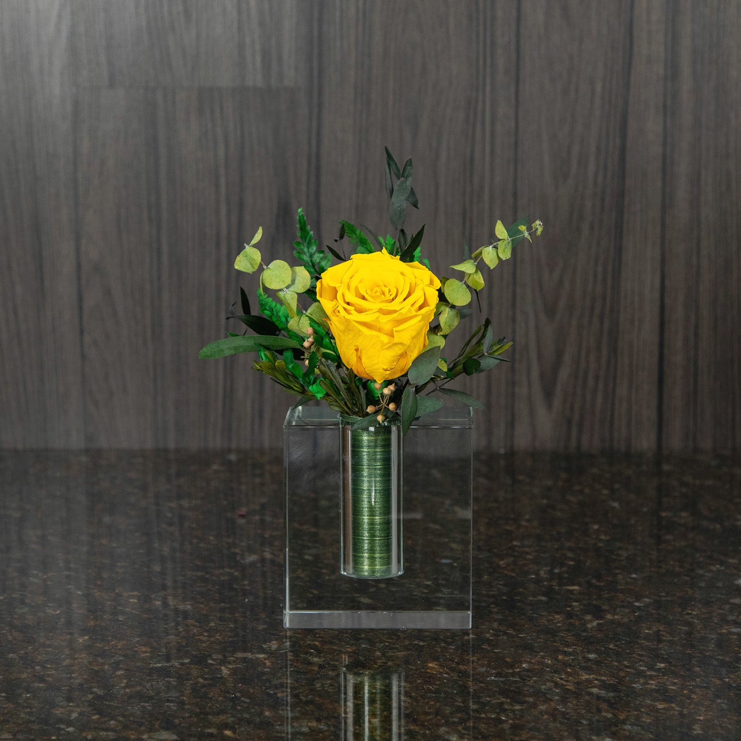 a single yellow preserved rose in a contemporary square glass vase with a bit of dried greenery