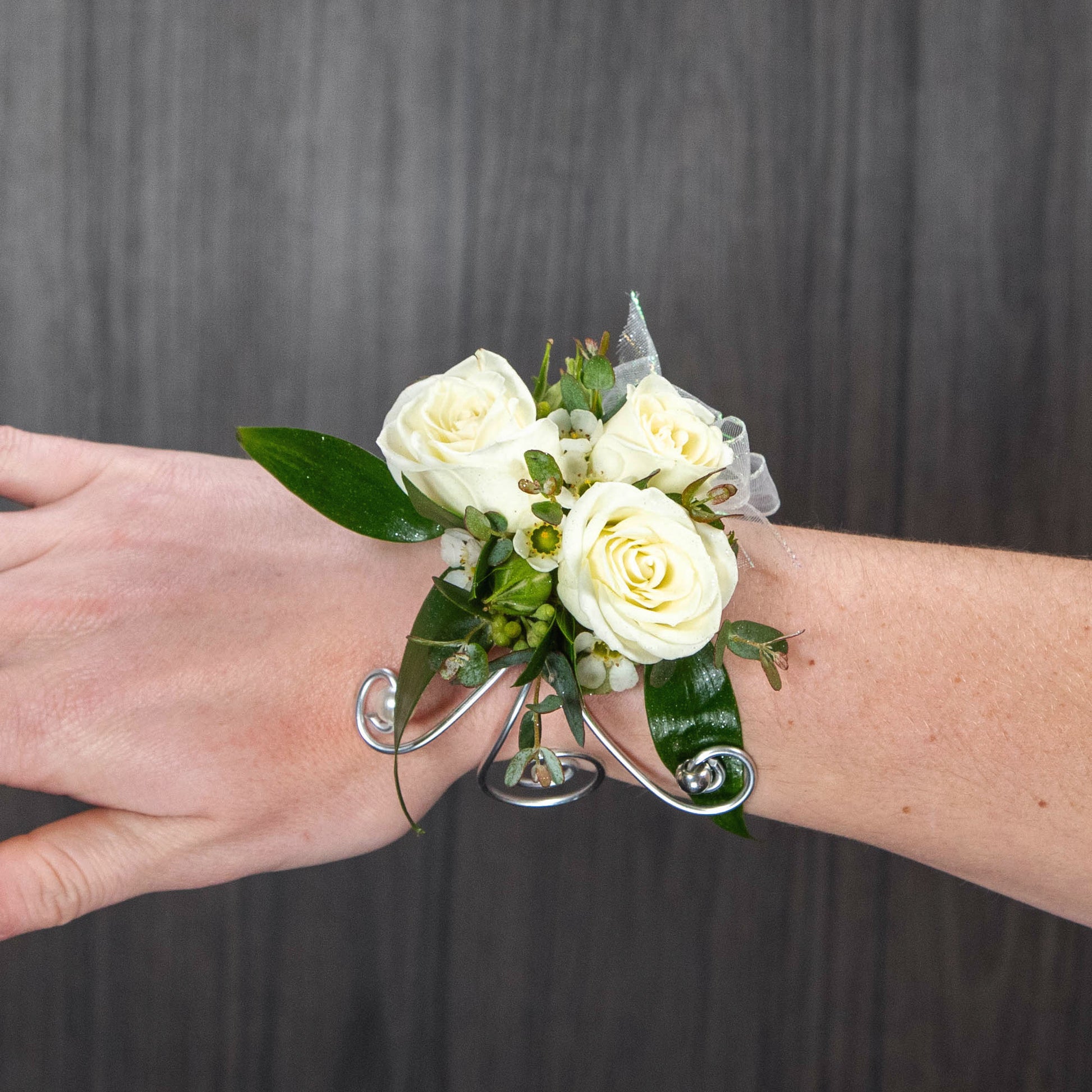a child size wrist corsage with white spray roses and purple waxflower