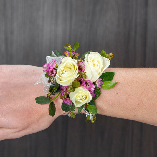 a child size wrist corsage with white spray roses and purple waxflower