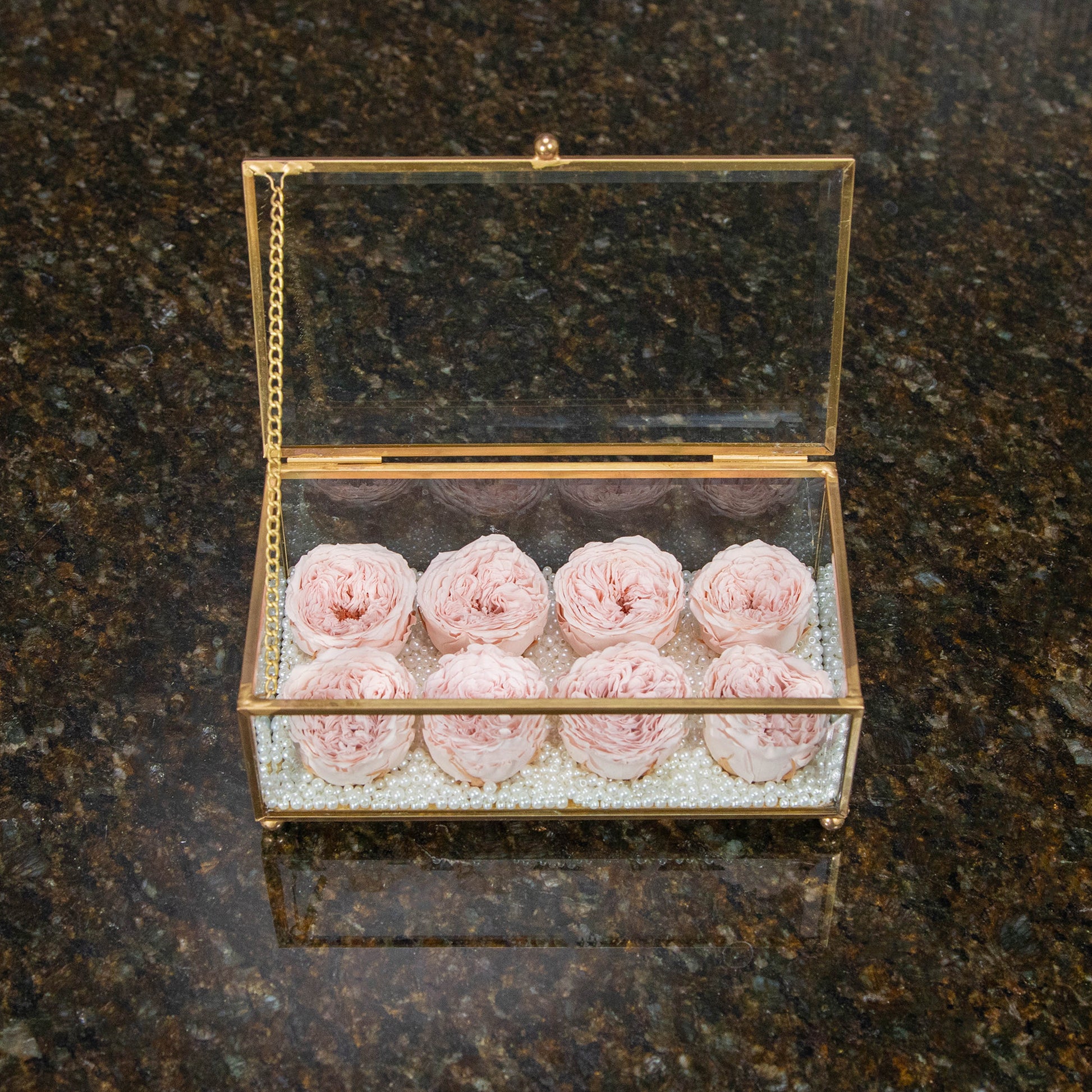 top down view of a glass box with 8 pink preserved roses inside with faux pearls lining the bottom