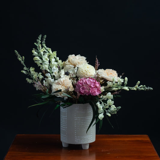 a mix of white dried flowers and a pop of pink in a white ceramic container
