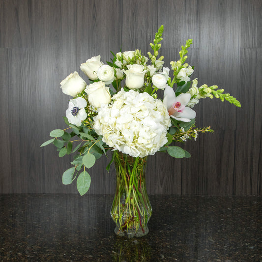 a tall flower arrangement with all white flowers in a glass vase