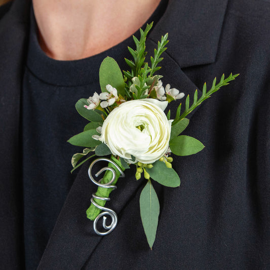 a white ranunculus boutonniere with white waxflower and different types of greenery