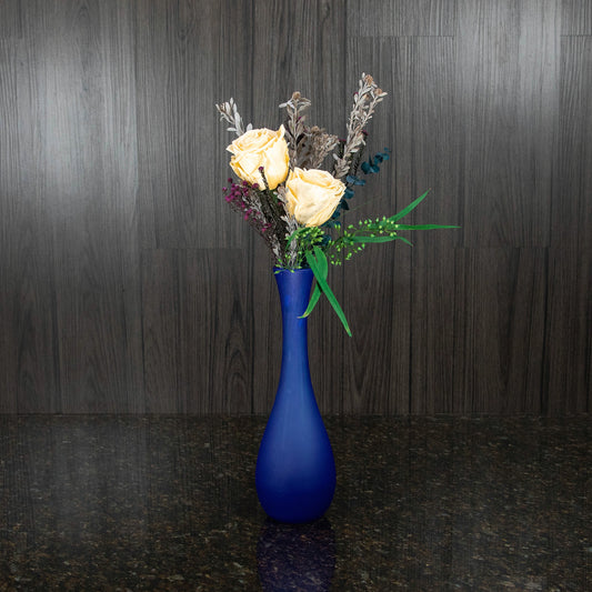 two cream preserved roses with greenery in a tall frosted blue glass vase